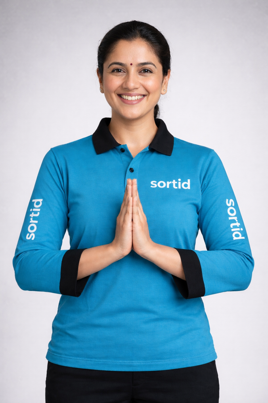 A smiling Sortid home cook in a turquoise Sortid uniform, greeting with a namaste